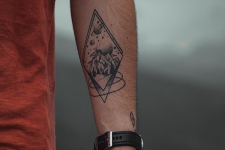 black and gray tattoo of a diamond shape encompassing a mountain and planets in space