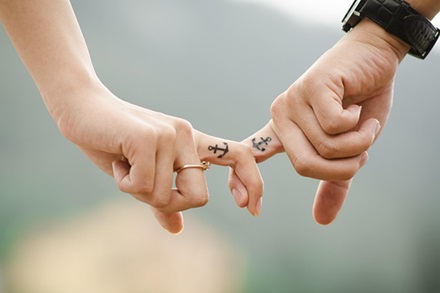 photo of two people holding hands with matching anchor tattoos on their fingers