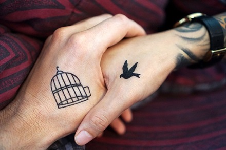 photo of two people holding hands, one with a bird cage and another with a bird tattoo on their respective hands