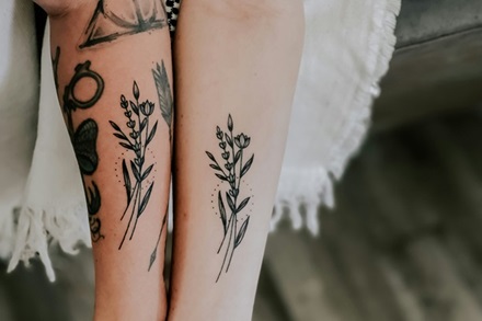 matching fine line flower tattoos on two different forearms